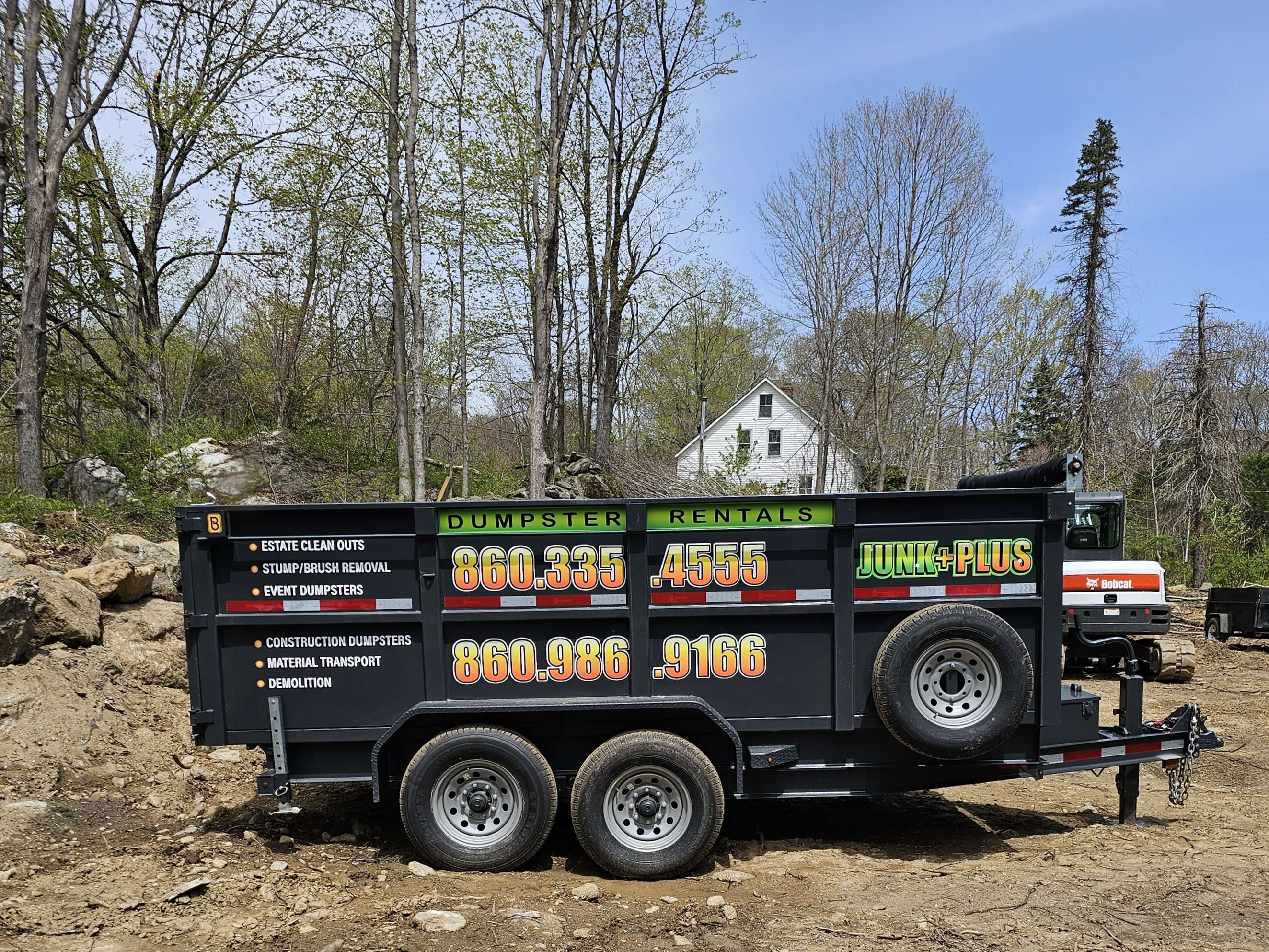 Junk Plus trailer dumpster in a tight-access wooded area.